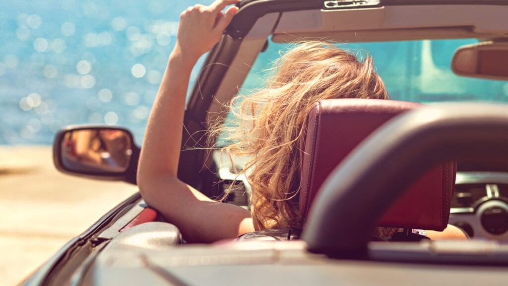 Person im Cabrio am Meer mit ausgestrecktem Arm