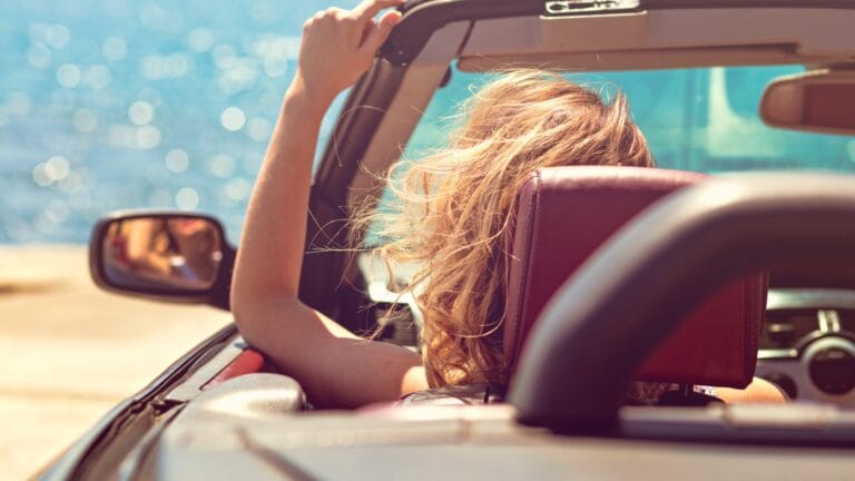 Person im Cabrio am Meer mit ausgestrecktem Arm